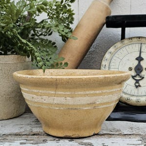 May include: A yellow ceramic mixing bowl with a wide rim and two horizontal white bands around the exterior. The bowl features a visible crack on the upper side and a fine network of surface crazing throughout the glazed finish.