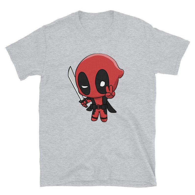 Puede incluir: Una camiseta gris con una imagen de dibujos animados de Deadpool sosteniendo una katana y haciendo un signo de paz. El personaje es rojo y negro con un ojo blanco.