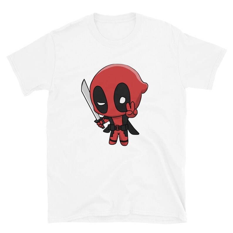 Puede incluir: Camiseta blanca con una imagen de dibujos animados de Deadpool sosteniendo una espada y haciendo un signo de paz. El personaje es rojo y negro con una m&aacute;scara blanca.