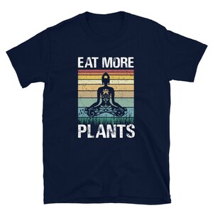 Pu&ograve; includere: T-shirt blu navy con una grafica in stile vintage di una persona che medita con il testo "Eat More Plants".