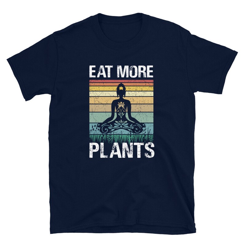 Pu&ograve; includere: T-shirt blu navy con una grafica in stile vintage di una persona che medita con il testo "Eat More Plants".