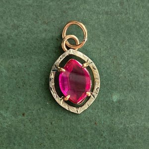 May include: A gold pendant with a marquise-cut, vibrant pink gemstone. The gemstone is set within a detailed, textured gold frame. The pendant has a small, looped bail for a chain.
