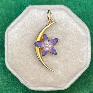 May include: A gold crescent moon charm with a purple flower enamel design. The flower has a white pearl center.