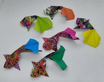 Może przedstawiać: Origami koi w różnych kolorach i wzorach. Korpusy ryb zdobią kwiatowe nadruki w kolorze czerwonym, fioletowym i czarnym, z płetwami w kolorze niebieskim, zielonym, pomarańczowym, różowym i żółtym. Te papierowe ryby są ułożone na białej powierzchni.