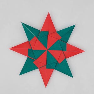Può includere: Una stella origami simmetrica composta da forme triangolari rosse e verde acqua. La stella ha otto punte, ognuna delle quali alterna il rosso e il verde acqua. L'artigianato di carta è ambientato su uno sfondo bianco.