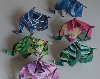 Może przedstawiać: Sześć origami słoni wykonanych z kolorowego papieru z wzorami. Słonie są w różnych pozach i ułożone są w półkole na białym tle.