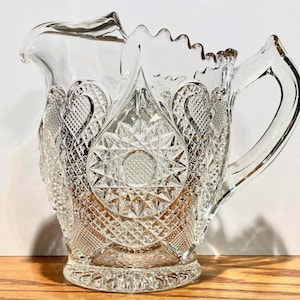 May include: A white ceramic mug with a black handle and the text "But First, Coffee" in a bold, black font. The mug is set against a blurred background, suggesting a cozy setting.