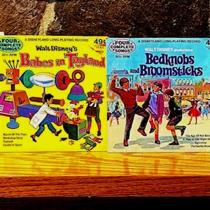 May include: A collection of vintage Walt Disney records, featuring colorful illustrations and titles like "20,000 Leagues Under the Sea," "Lambert the Sheepish Lion," and "Babes in Toyland." The records are displayed on a wooden shelf.