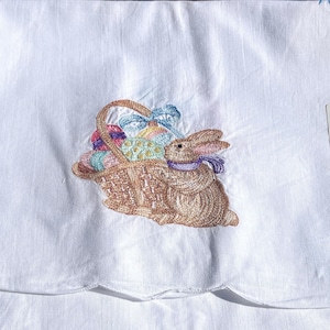 May include: White embroidered kitchen towel with a brown bunny carrying a basket of colorful Easter eggs.