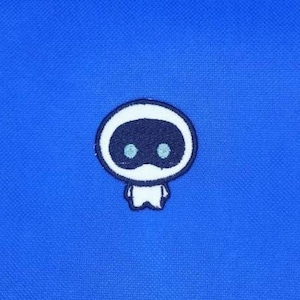 May include: A blue fabric with a small, white-outlined cartoon character patch. The character has a dark blue oval head with two dark blue eye shapes and a small white body.