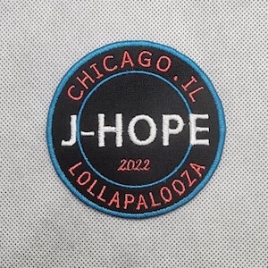 May include: A blue and red circular patch with the text "CHICAGO, IL" and "LOLLAPALOOZA" around a black circle with the text "J-HOPE" and "2022" inside.