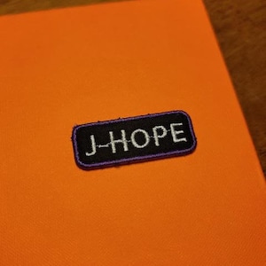 May include: A purple and black embroidered patch with the text "J-HOPE" in white.