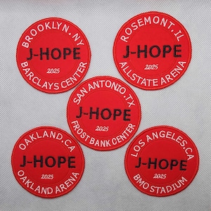 May include: Five red circular patches with white text and black lettering. Each patch features the text "J-HOPE" and the year "2025". The patches also include the names of different arenas, including Barclays Center, Allstate Arena, Frost Bank Center, Oakland Arena, and BMO Stadium.