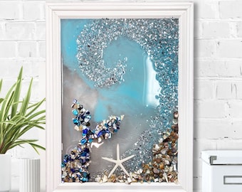 May include: A framed artwork featuring a mermaid tail made of blue and white stones, a white starfish, and a sparkling, textured background in shades of blue and silver. The artwork is encased in a white frame.