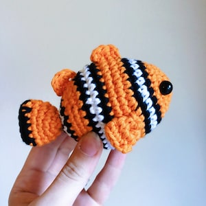 May include: A crocheted orange, white, and black clownfish toy with black button eyes.