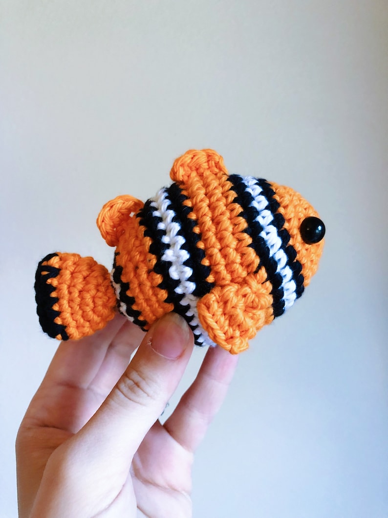May include: A crocheted orange, white, and black clownfish toy with black button eyes.