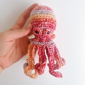 May include: A crocheted octopus toy with a red, orange, and purple color gradient. The octopus has eight tentacles and large, black eyes.