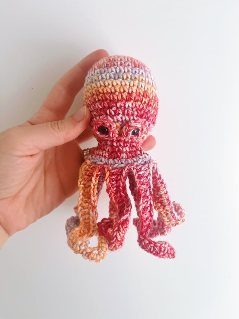 May include: A crocheted octopus toy with a red, orange, and purple color gradient. The octopus has eight tentacles and large, black eyes.