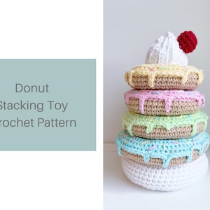 May include: A crocheted donut stacking toy with a white frosting and red cherry on top. The donuts are stacked in a tower with different colored frosting and sprinkles.