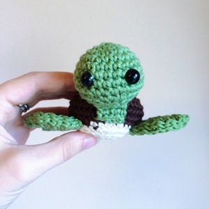May include: A crocheted green sea turtle with brown and white accents and black eyes.