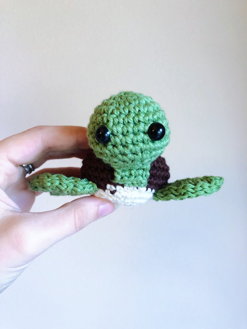 May include: A crocheted green sea turtle with brown and white accents and black eyes.