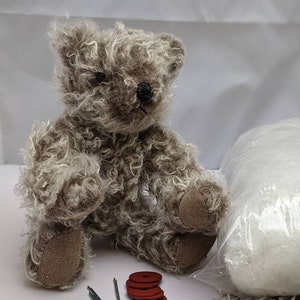 May include: A brown and white mohair teddy bear kit. The kit includes stuffing, two black eyes, four red felt paw pads, two metal safety eyes, and two metal washers.