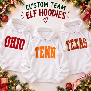 May include: Three white hooded sweatshirts with white pom-pom drawstrings. The left hoodie features the red text OHIO, the center hoodie features the orange text TENN, and the right hoodie features the brown text TEXAS. Above the hoodies, the text reads CUSTOM TEAM ELF HOODIES.