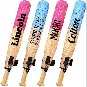 May include: Four baseball bats with a unique ice cream cone design. The top of each bat is decorated with pink and blue sprinkles, and the names "Lincoln", "Sully", "Macie", and "Colton" are printed on them. The bats have a wooden handle and a black strap.
