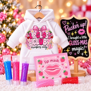 May include: A white hoodie with a pink and red graphic reading Lipgloss Club members only, a lip mask packet, and five glittery lip gloss tubes. A wooden sign displays the text Pucker up! I brought a little GLOSS-MAS magic! in pink and white.