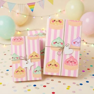 May include: Two rectangular gift boxes wrapped in light pink and white striped paper featuring a repeating pattern of smiling, colorful dumpling characters. Each box is tied with thin twine and adorned with a small, plain white paper gift tag.