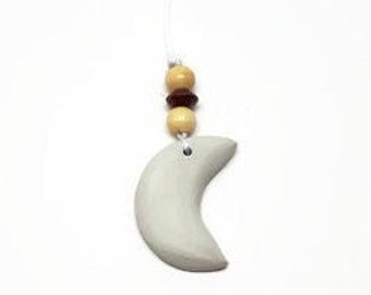 Peut inclure: Un charme en forme de croissant de lune blanc suspendu à une ficelle avec des perles en bois brun et beige.