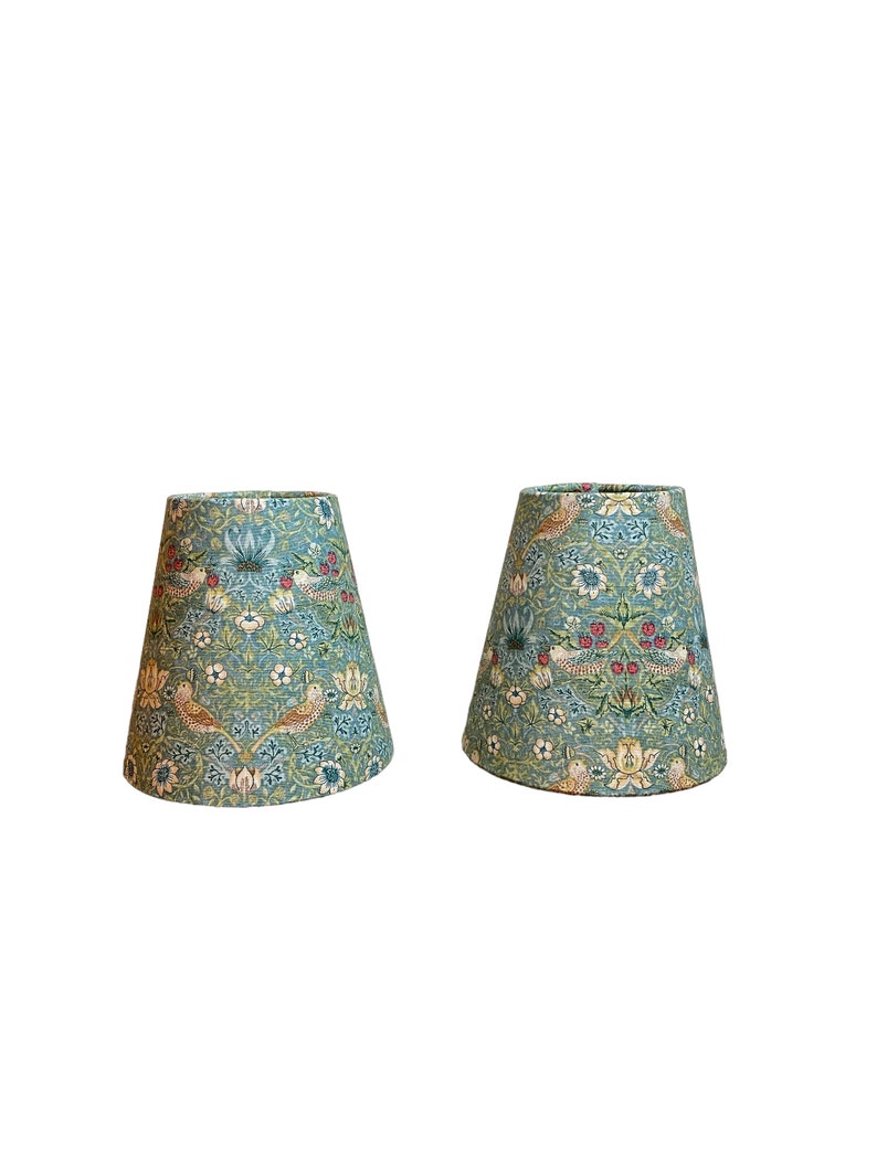 May include: Two teal blue lampshades with a floral and bird pattern. The pattern features small red berries, white flowers, and brown birds.