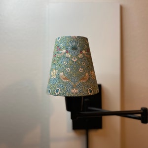 May include: A black wall-mounted lamp with a blue and white patterned lampshade. The lampshade has a floral design with birds.