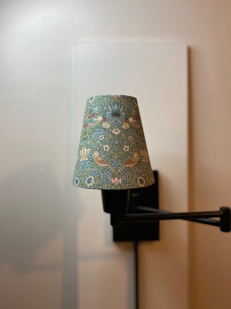May include: A black wall-mounted lamp with a blue and white patterned lampshade. The lampshade has a floral design with birds.