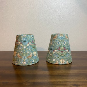 May include: Two lampshades with a floral pattern in shades of green, blue, red, and yellow. The lampshades are made of fabric and have a conical shape.