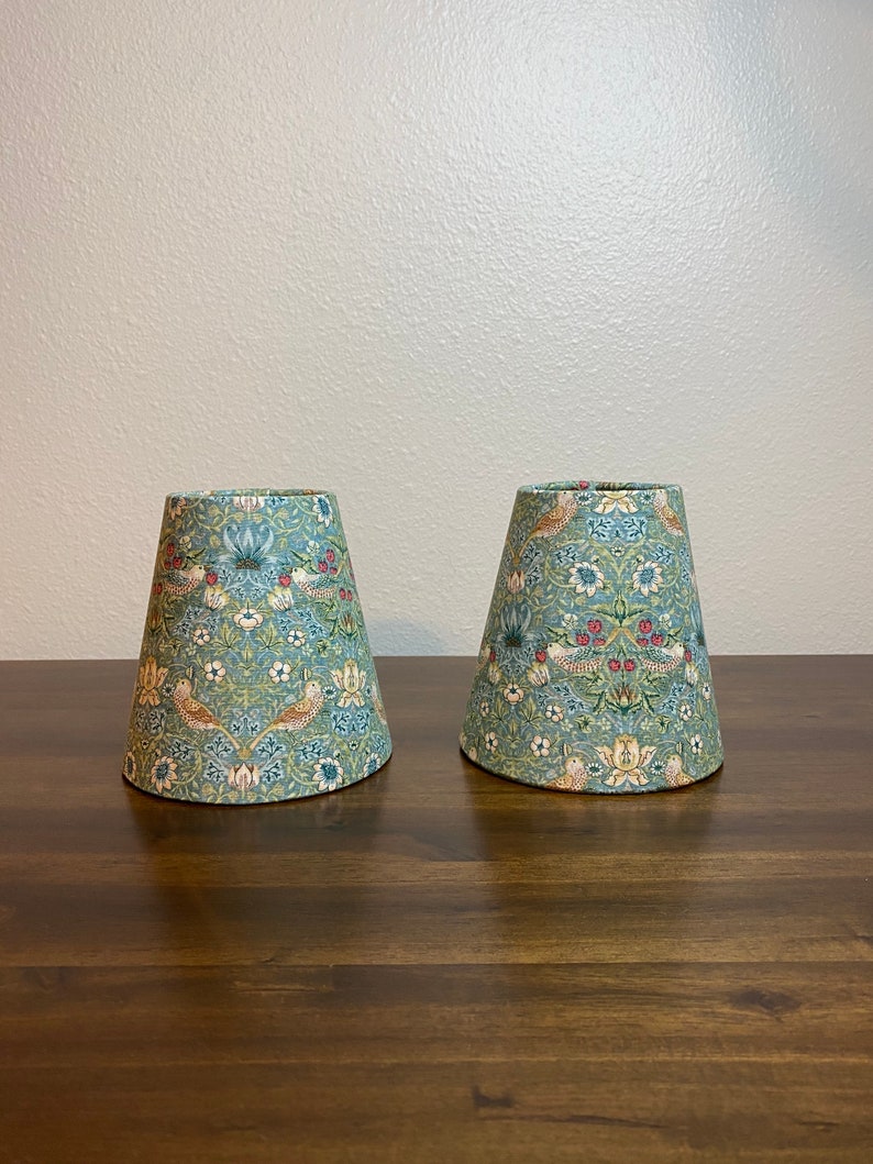 May include: Two lampshades with a floral pattern in shades of green, blue, red, and yellow. The lampshades are made of fabric and have a conical shape.