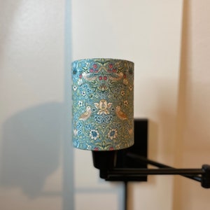 May include: A black wall-mounted lamp with a blue and white patterned fabric lampshade. The lampshade features a floral design with birds.