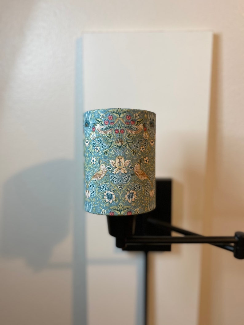 May include: A black wall-mounted lamp with a blue and white patterned fabric lampshade. The lampshade features a floral design with birds.