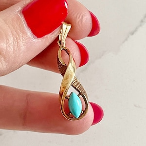 May include: A gold pendant with a turquoise stone in the center. The pendant is shaped like an infinity symbol.
