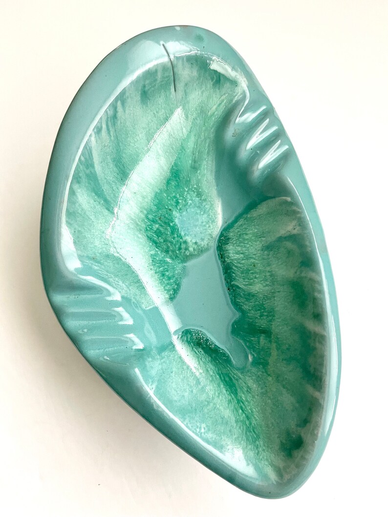 May include: A light green ceramic ashtray with a swirl design. The ashtray is shaped like a leaf and has a wide, shallow bowl.