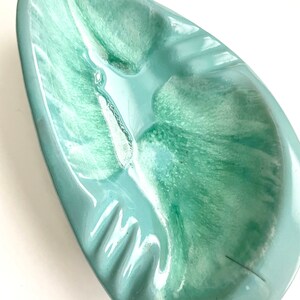 May include: A light blue ceramic ashtray with a swirl pattern. The ashtray has a rounded, oval shape with a wide, shallow well.