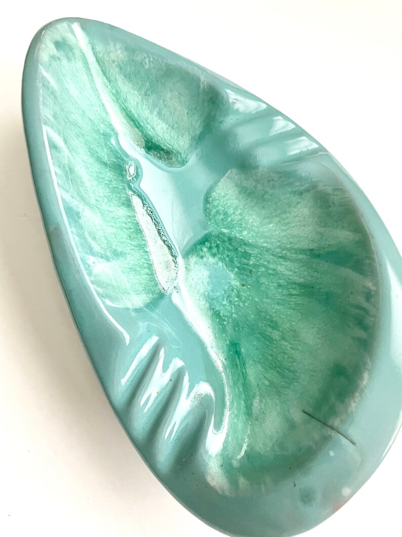 May include: A light blue ceramic ashtray with a swirl pattern. The ashtray has a rounded, oval shape with a wide, shallow well.