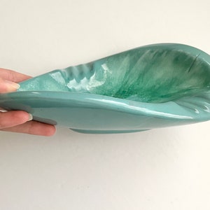 May include: A light blue ceramic bowl with a swirl pattern in shades of green and white. The bowl has a unique, asymmetrical shape.