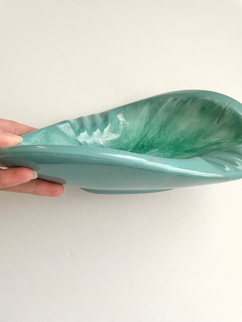 May include: A light blue ceramic bowl with a swirl pattern in shades of green and white. The bowl has a unique, asymmetrical shape.