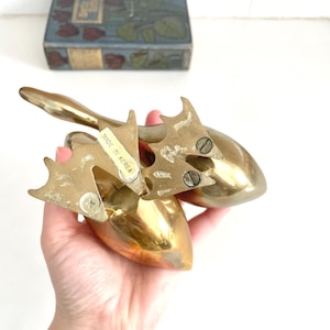 May include: A pair of vintage brass duck figurines with a shiny, golden finish. The ducks have detailed wings and feet, with a label that reads "MADE IN KOREA". The figurines are likely decorative items.