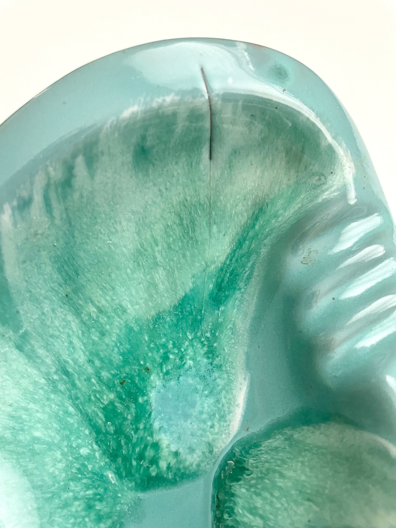 May include: A light blue ceramic ashtray with a green and white marbled glaze. The ashtray has a deep, rounded bowl with a slightly raised rim.