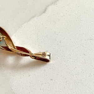 May include: Close-up of the back of a gold pendant with the markings "14K" and "585" on the clasp.