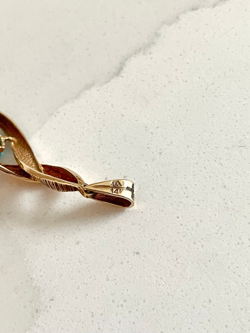 May include: Close-up of the back of a gold pendant with the markings "14K" and "585" on the clasp.