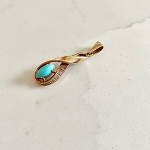 May include: A gold pendant with a turquoise stone set in a twisted design.