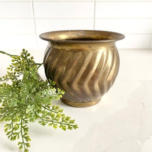 Pode incluir: Um vaso de latão dourado com um design canelado. O vaso é redondo e tem uma abertura larga.